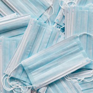 Top view of many clean single use light blue surgical protective face mask lying on top of each other in disorder